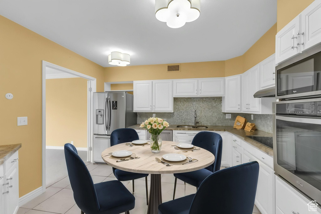 Kitchen featuring stainless steel appliances, a sink, decorative backsplash, white cabinetry, and light tile patterned floors