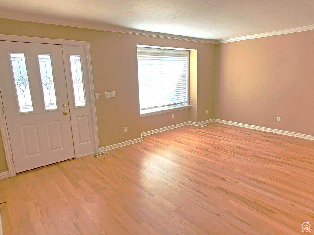 Foyer entrance featuring light wood-type flooring, baseboards, visible vents, and ornamental molding