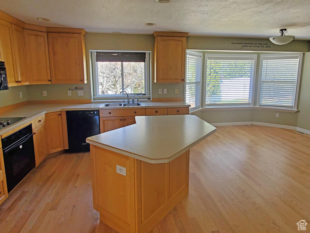 Kitchen with black appliances, light countertops, light wood-style floors, a textured ceiling, and a sink