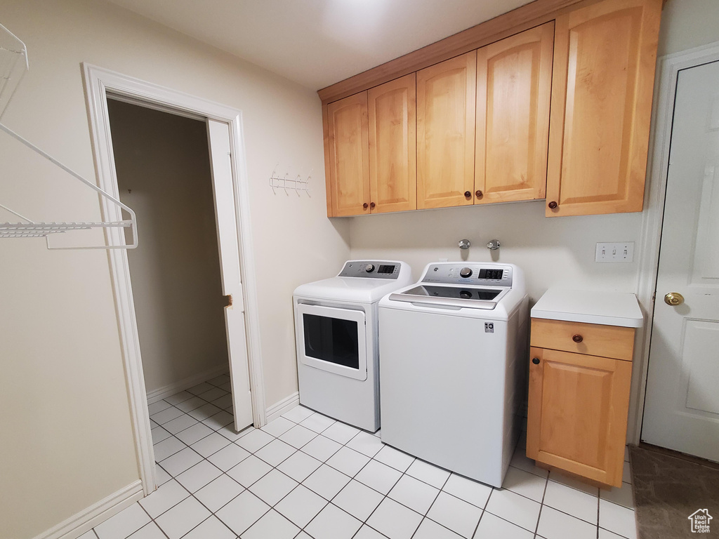 Clothes washing area with cabinet space, light tile patterned floors, independent washer and dryer, and baseboards