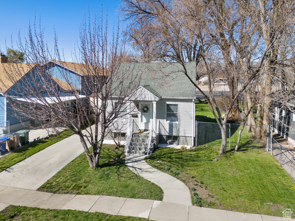View of front of house with concrete driveway, a shingled roof, a front yard, and fence