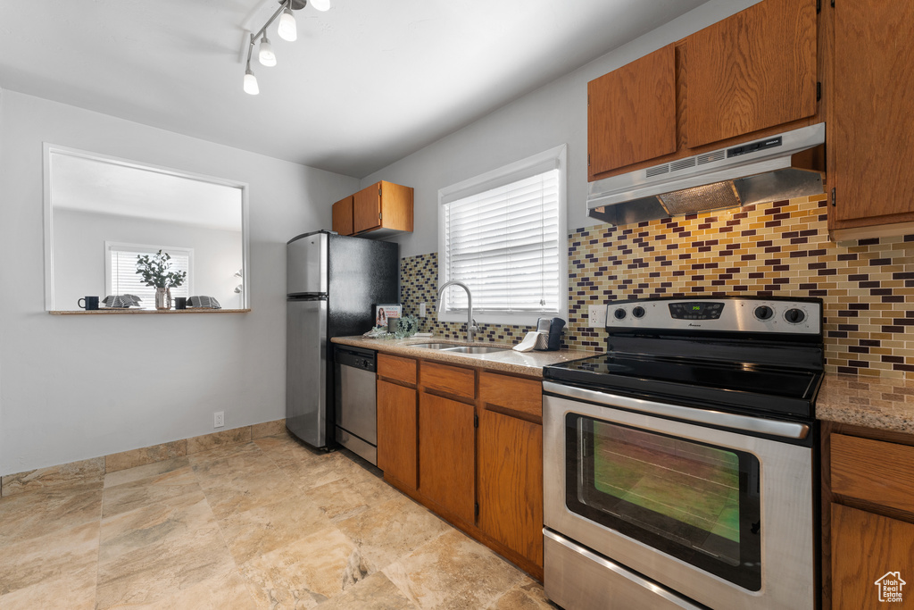 Kitchen featuring a sink, appliances with stainless steel finishes, under cabinet range hood, tasteful backsplash, and brown cabinets