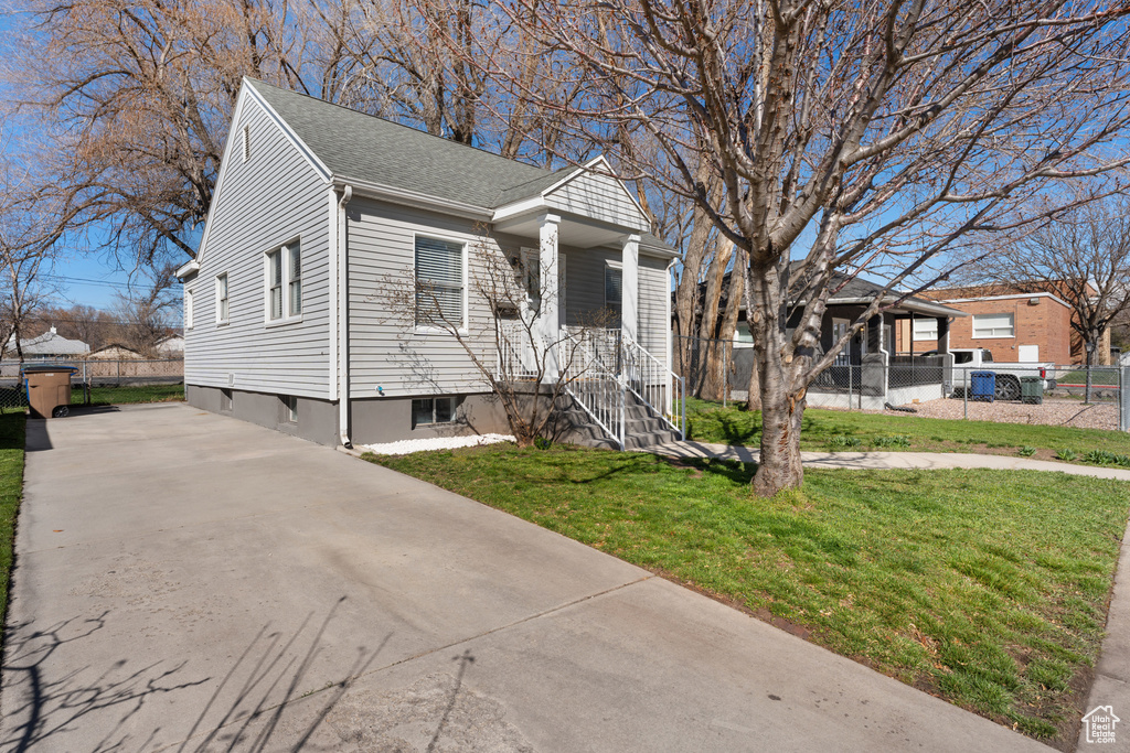 View of front of home with concrete driveway, fence, a front yard, and a shingled roof