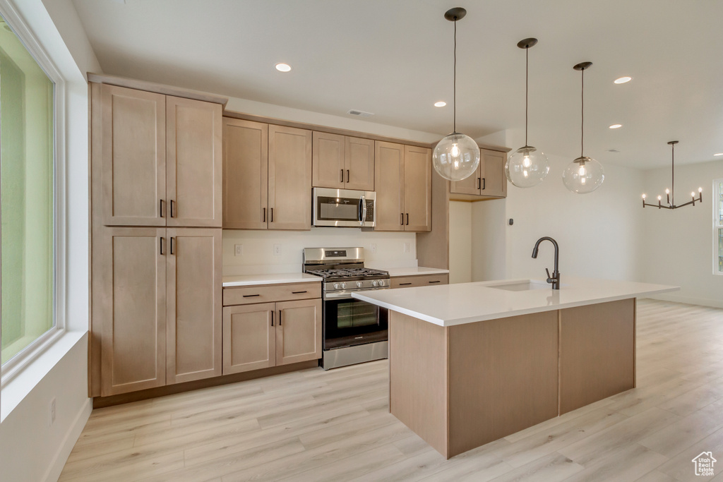 Kitchen with stainless steel appliances, light wood-style flooring, light countertops, and a sink