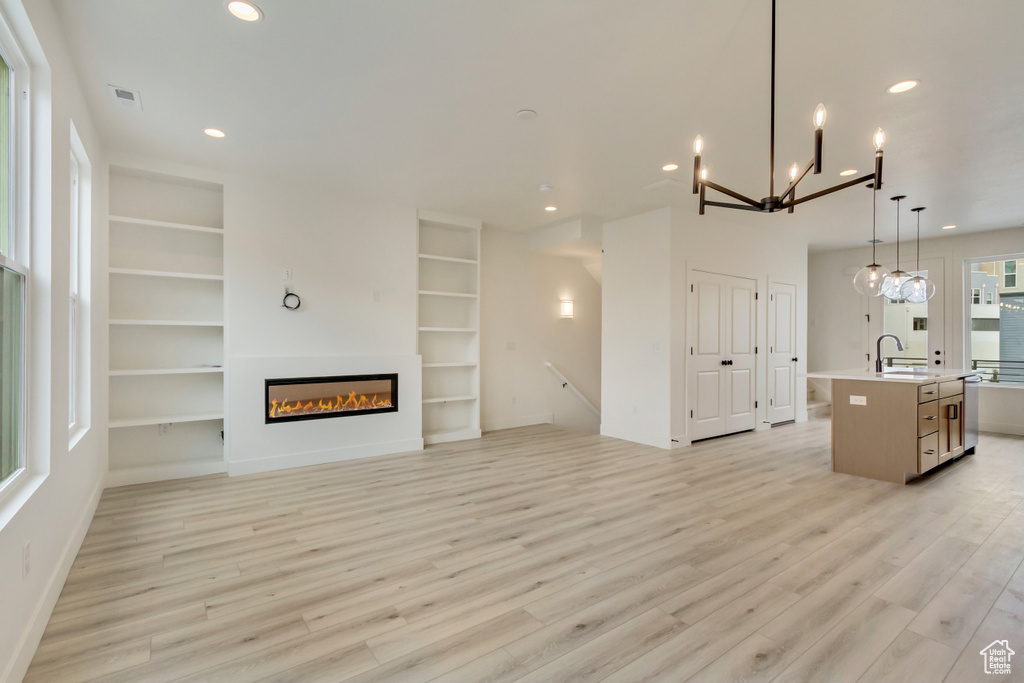 Unfurnished living room featuring light wood-style flooring, a sink, recessed lighting, and built in shelves