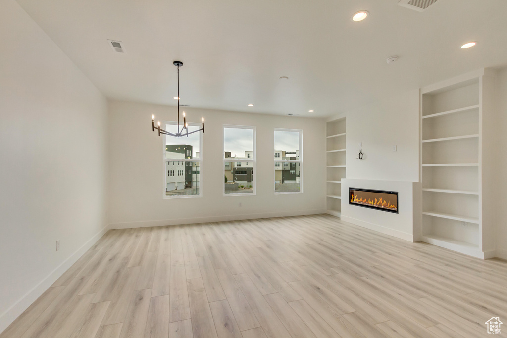 Unfurnished living room with baseboards, a glass covered fireplace, an inviting chandelier, and light wood-style floors