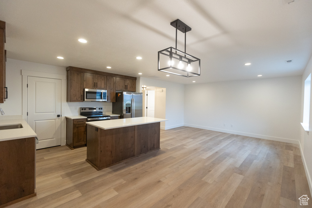 Kitchen featuring light wood-style flooring, a sink, stainless steel appliances, light countertops, and a center island