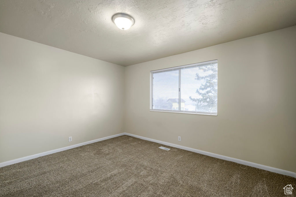 Carpeted empty room featuring visible vents, baseboards, and a textured ceiling