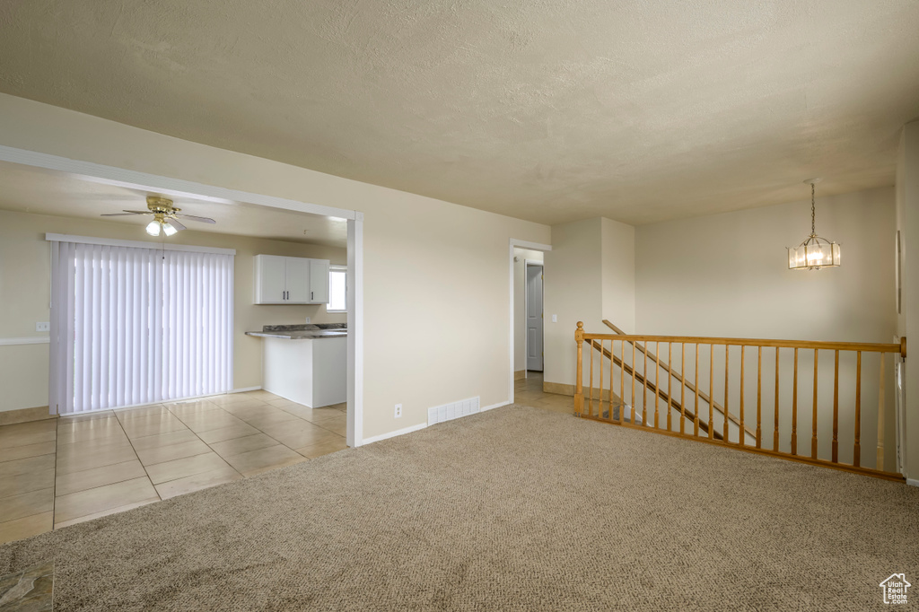 Spare room with visible vents, light carpet, ceiling fan with notable chandelier, a textured ceiling, and light tile patterned floors