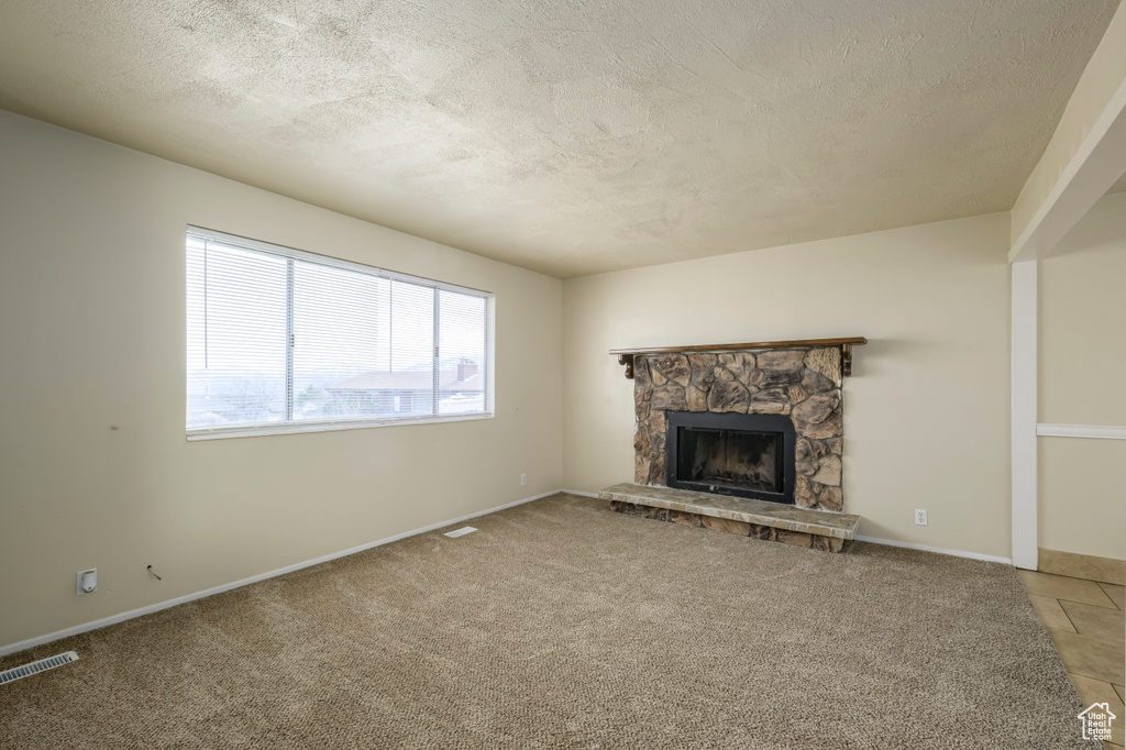 Unfurnished living room with visible vents, a textured ceiling, a stone fireplace, and light colored carpet