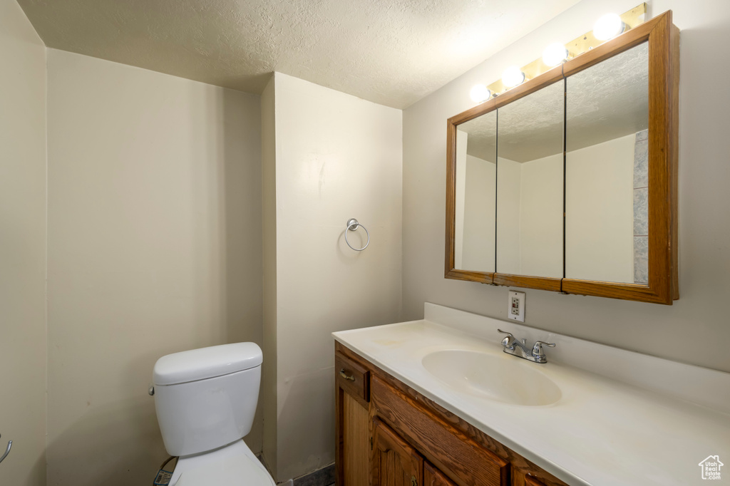 Half bathroom featuring a textured ceiling, vanity, and toilet