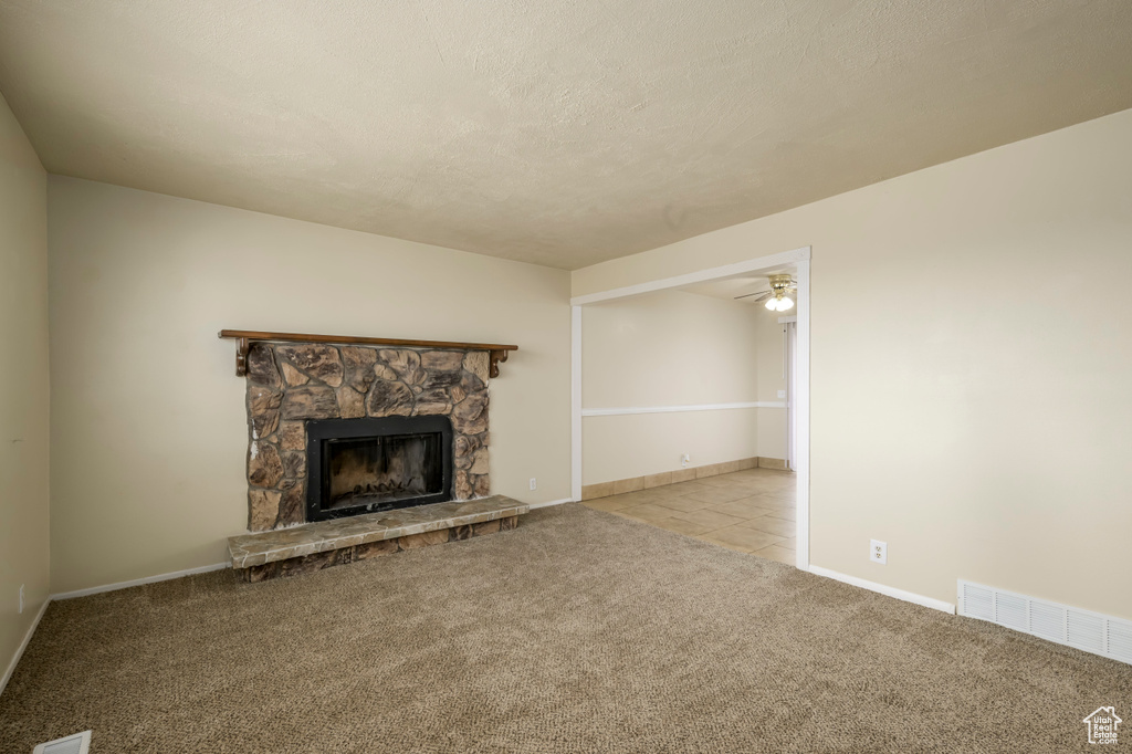 Unfurnished living room with a ceiling fan, visible vents, a stone fireplace, tile patterned flooring, and carpet flooring