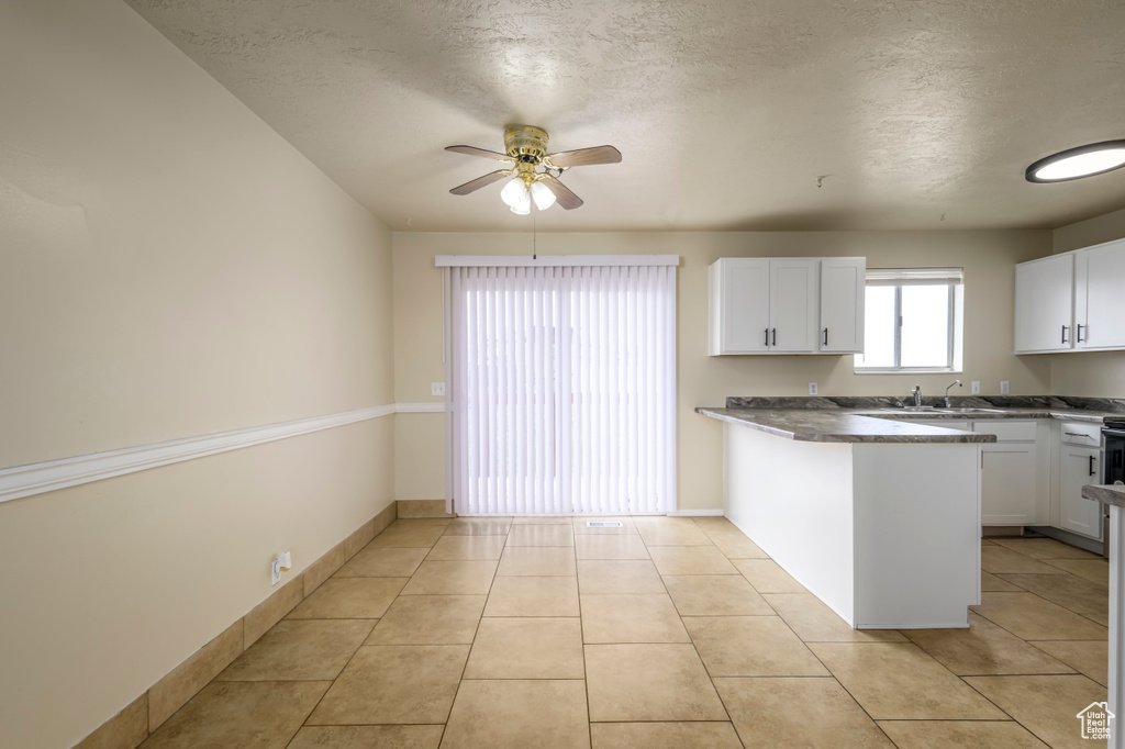 Kitchen with light tile patterned flooring, a peninsula, white cabinetry, and a ceiling fan