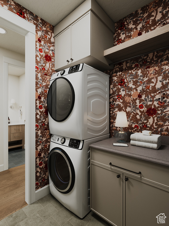Laundry room featuring stacked washer / dryer, wallpapered walls, cabinet space, and light tile patterned floors