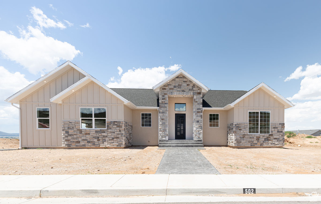 View of front of home with board and batten siding, stone siding, and roof with shingles