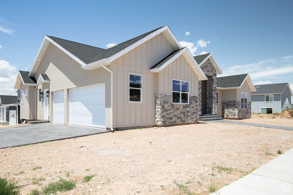 View of front of house with board and batten siding, a garage, driveway, roof with shingles, and stone siding