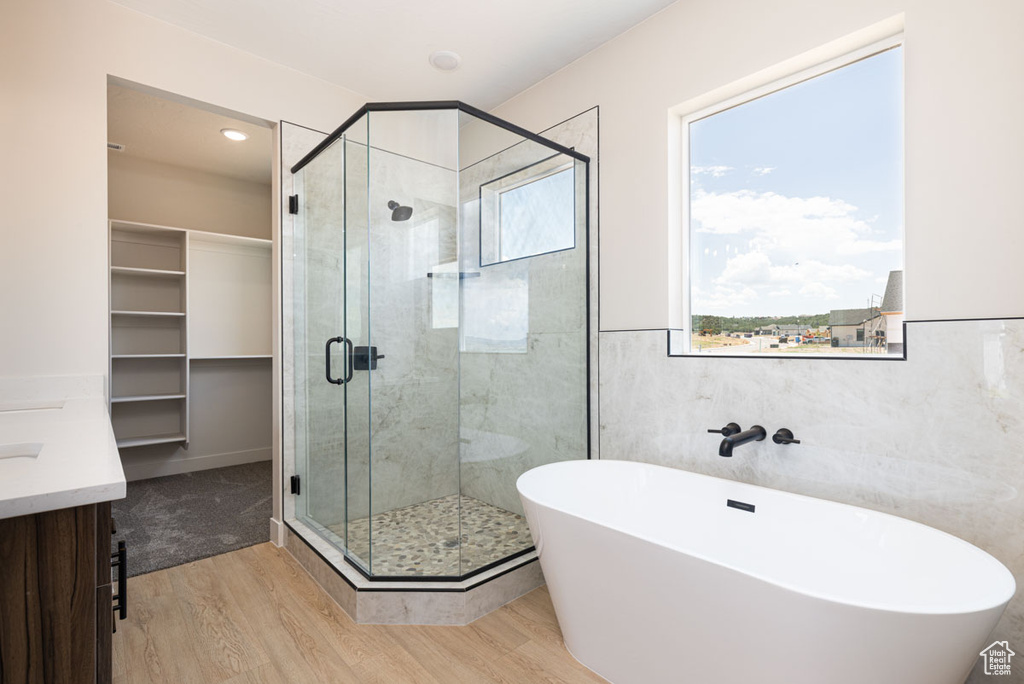 Full bathroom with wood finished floors, a shower stall, a soaking tub, vanity, and tile walls