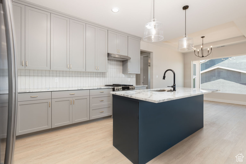 Kitchen featuring gray cabinetry, light wood finished floors, under cabinet range hood, a chandelier, and light stone counters