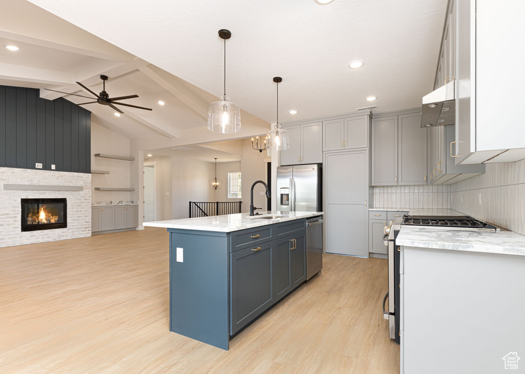 Kitchen featuring appliances with stainless steel finishes, light wood-style floors, under cabinet range hood, open floor plan, and a kitchen island with sink