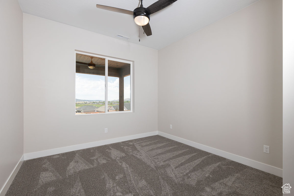 Empty room with dark colored carpet and a ceiling fan