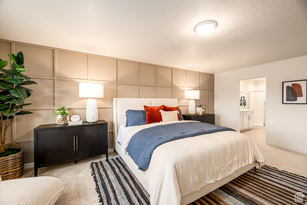 Bedroom with baseboards, light carpet, ensuite bathroom, a textured ceiling, and a decorative wall