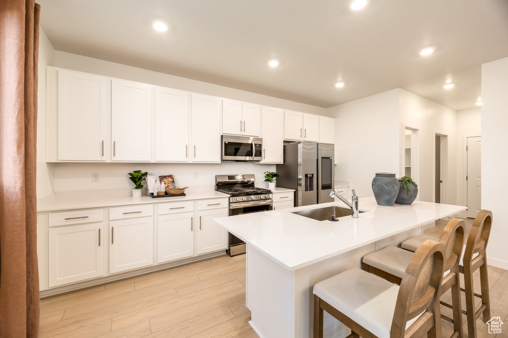 Kitchen featuring appliances with stainless steel finishes, white cabinetry, a kitchen breakfast bar, and a sink