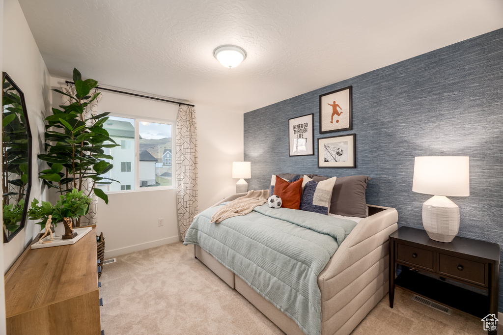 Bedroom with baseboards, visible vents, carpet floors, wallpapered walls, and an accent wall