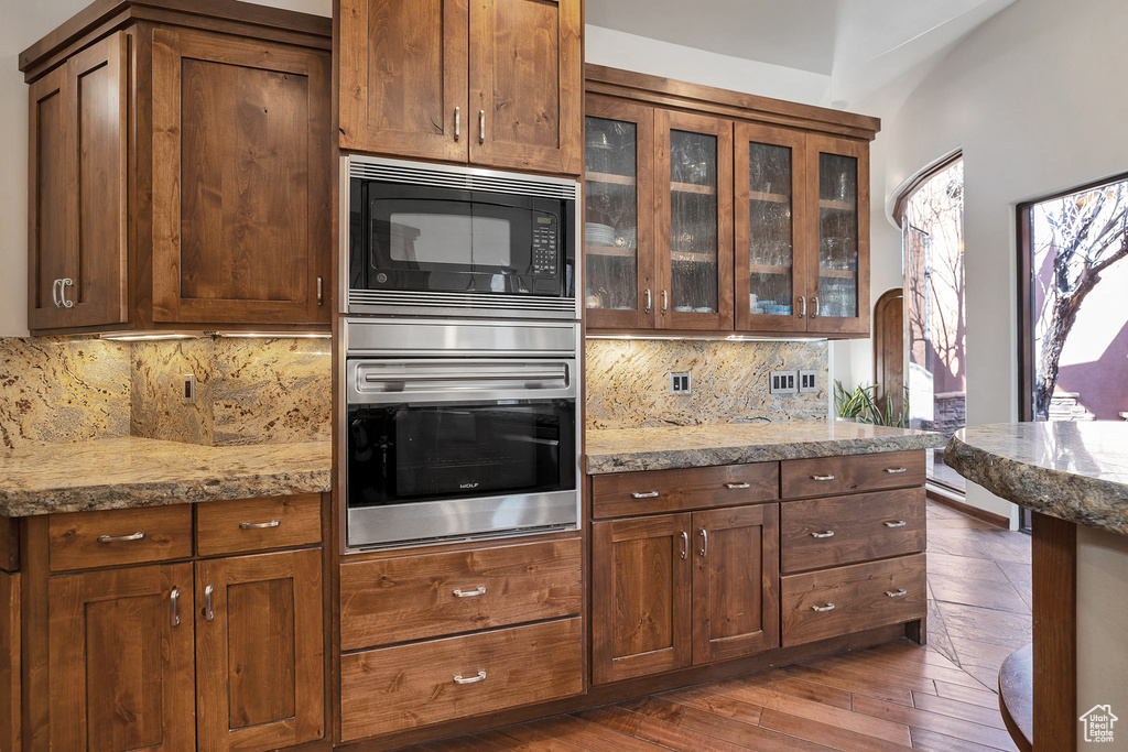 Kitchen featuring tasteful backsplash, dark wood-type flooring, glass insert cabinets, oven, and black microwave