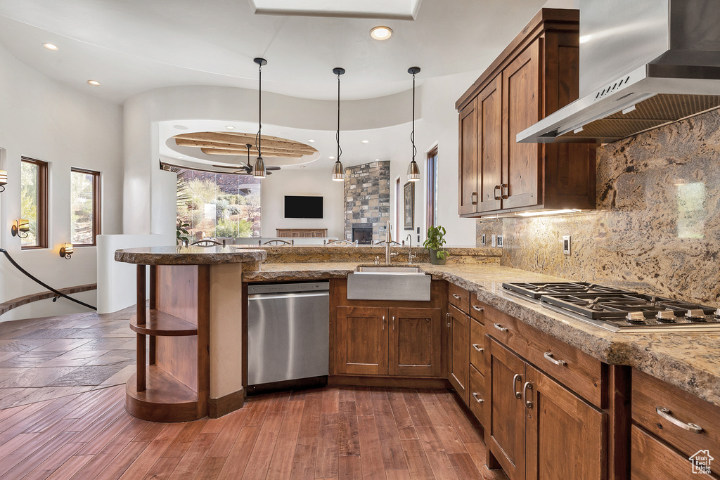 Kitchen with a peninsula, a sink, decorative backsplash, appliances with stainless steel finishes, and wall chimney range hood