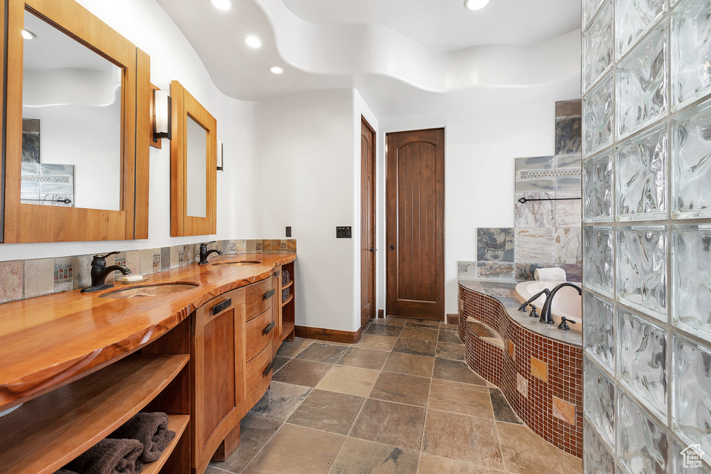Full bathroom with stone tile flooring, recessed lighting, baseboards, a bath, and vanity