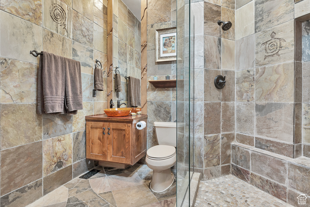 Bathroom featuring tile walls, toilet, tiled shower, and vanity