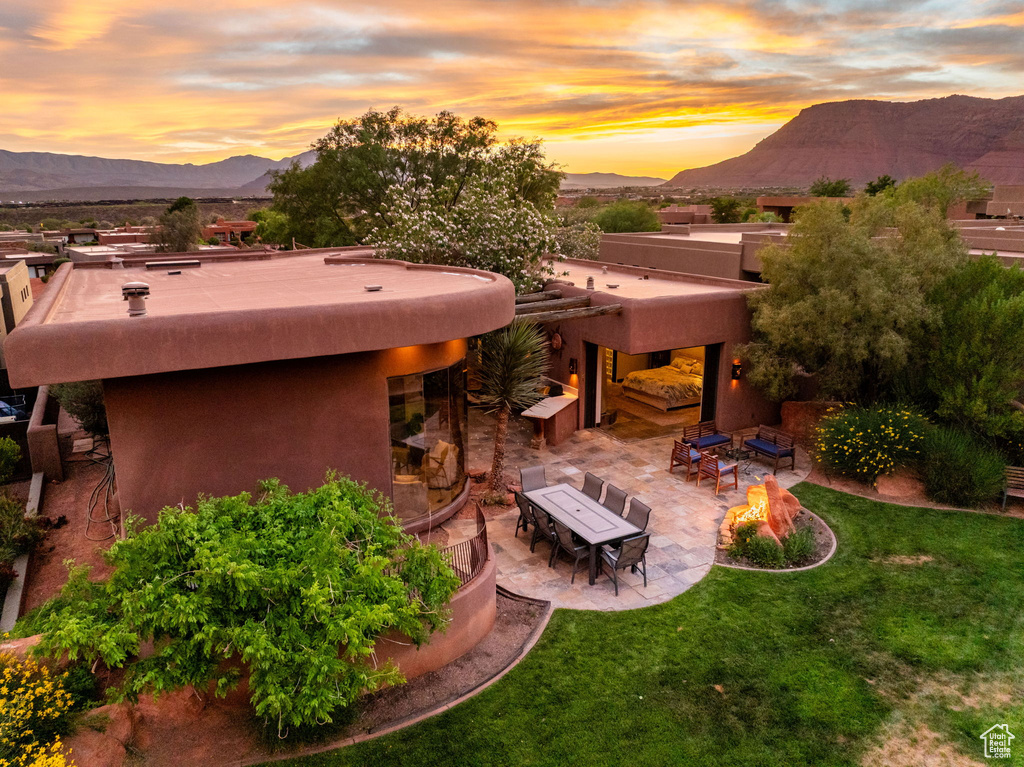 Rear view of property featuring a mountain view, a patio, a lawn, stucco siding, and an outdoor fire pit