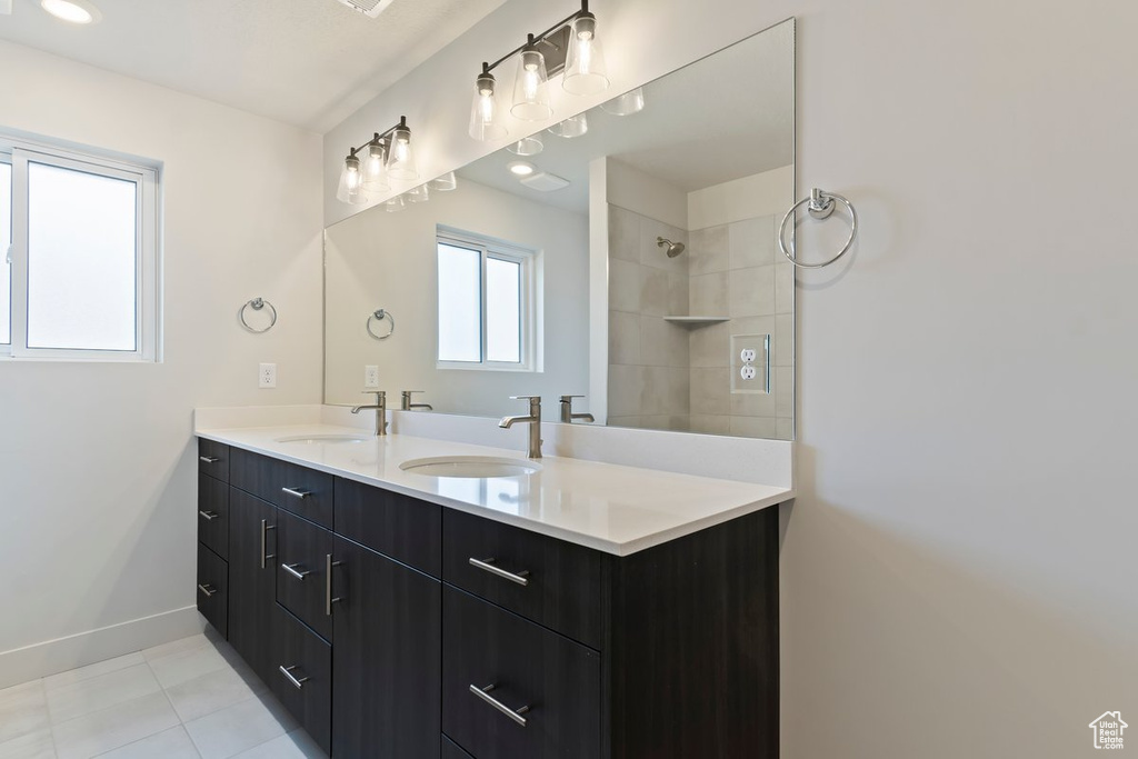 Full bathroom featuring double vanity, a tile shower, baseboards, and a sink