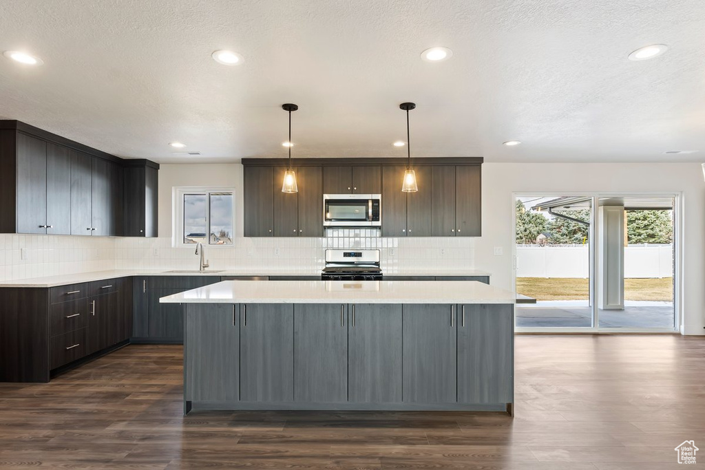 Kitchen featuring a sink, a kitchen island, dark wood-style floors, appliances with stainless steel finishes, and light countertops