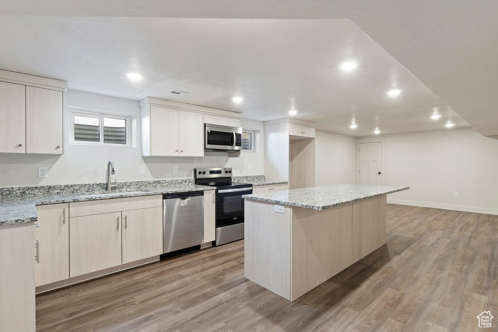 Kitchen featuring appliances with stainless steel finishes, a center island, light wood-style floors, and a sink