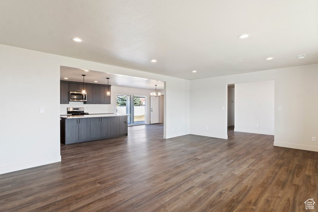 Unfurnished living room featuring recessed lighting, dark wood-style floors, baseboards, and a chandelier