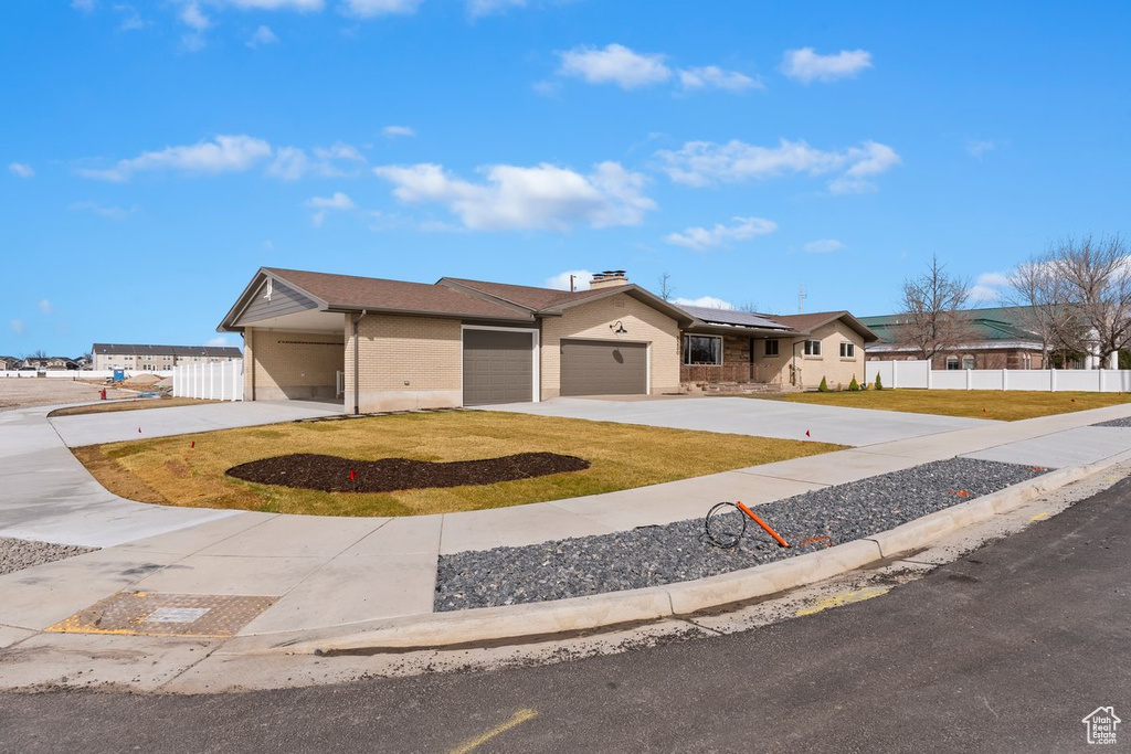 Ranch-style home with a front lawn, driveway, fence, an attached garage, and solar panels