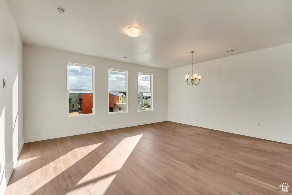 Empty room with baseboards, wood finished floors, and a chandelier