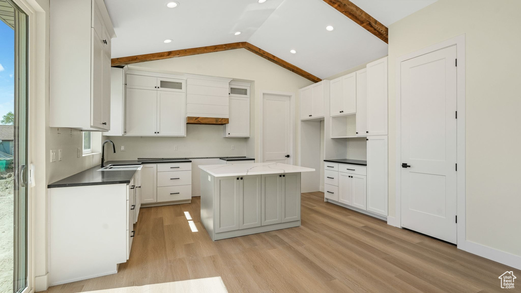 Kitchen with light wood finished floors, a center island, vaulted ceiling, white cabinets, and recessed lighting