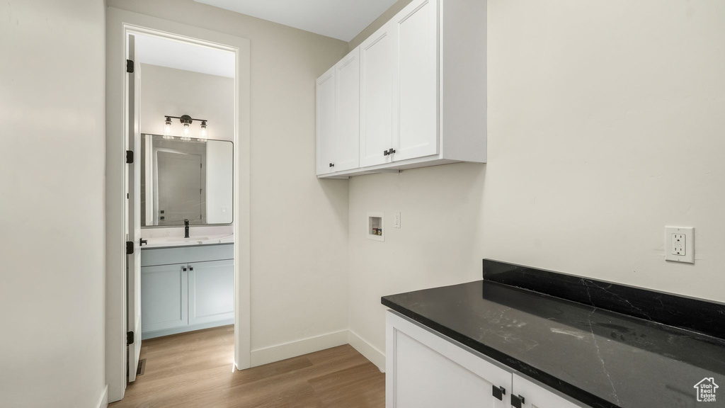 Laundry area with light wood finished floors, washer hookup, and cabinet space