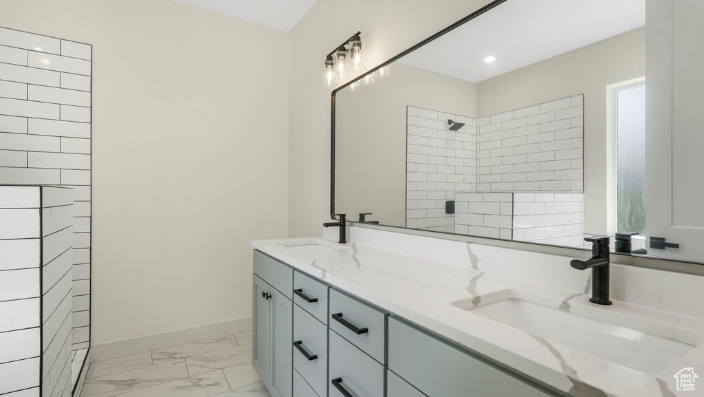 Bathroom featuring marble look tile flooring, double vanity, tiled shower, and recessed lighting