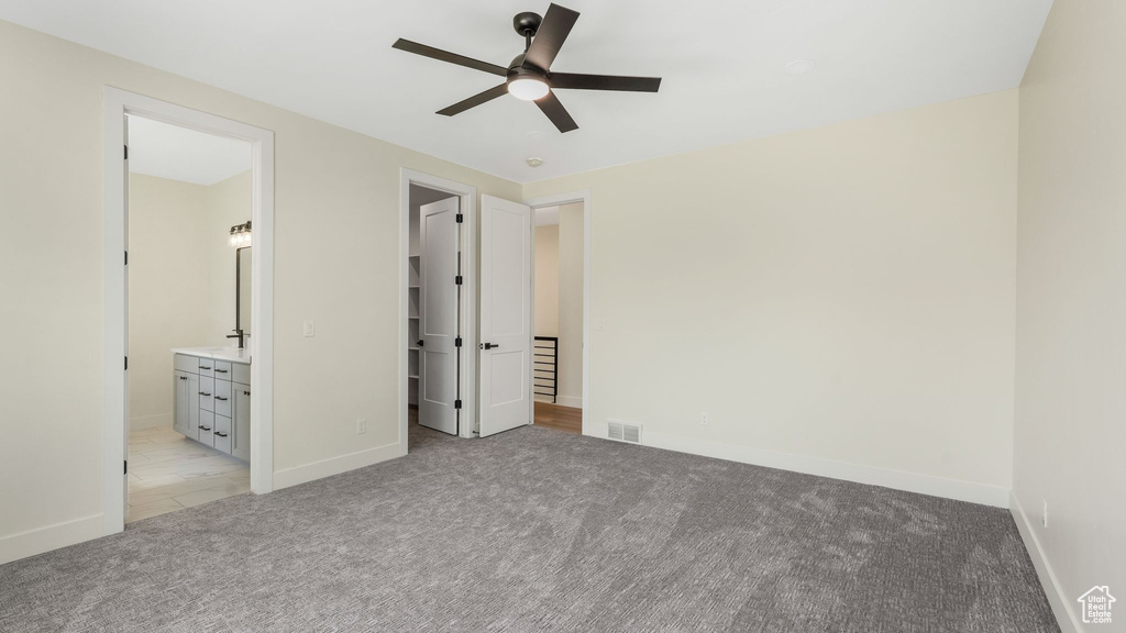 Unfurnished bedroom with light carpet, a spacious closet, ensuite bathroom, and a ceiling fan