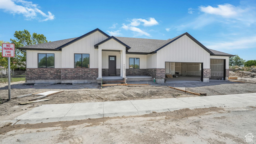Modern inspired farmhouse with a garage, roof with shingles, brick siding, board and batten siding, and driveway