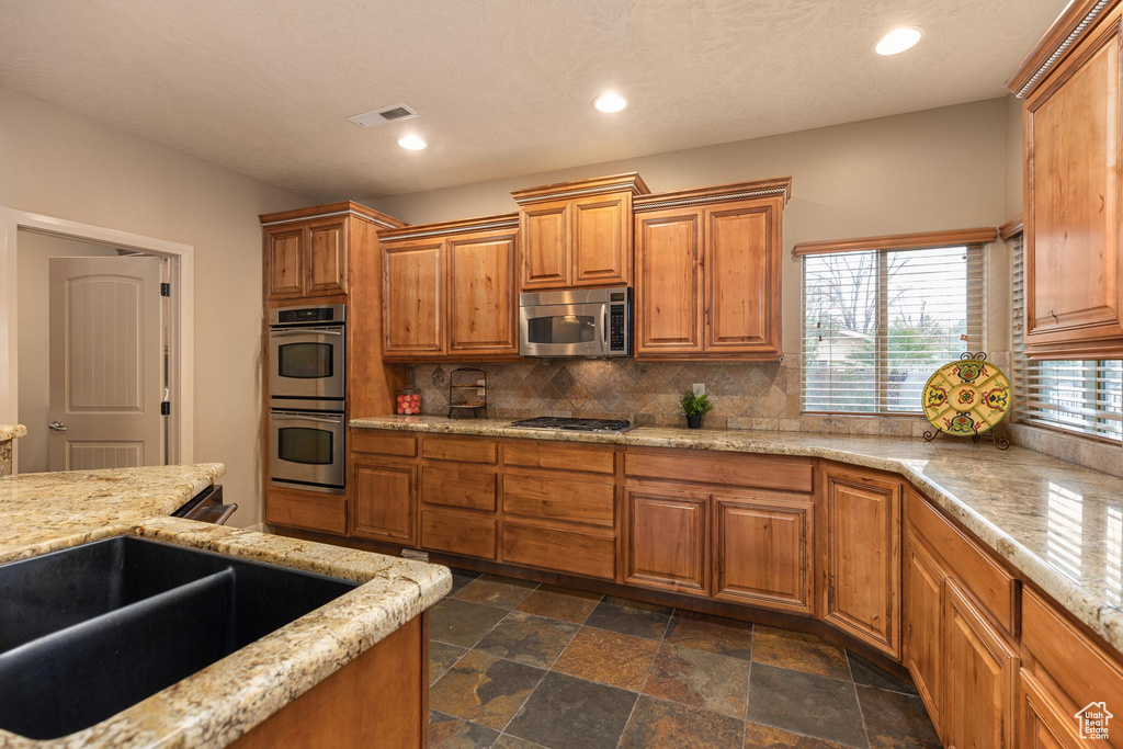 Kitchen with visible vents, backsplash, recessed lighting, brown cabinetry, and stainless steel appliances