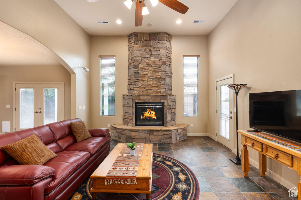 Living area with arched walkways, a stone fireplace, a wealth of natural light, and a ceiling fan