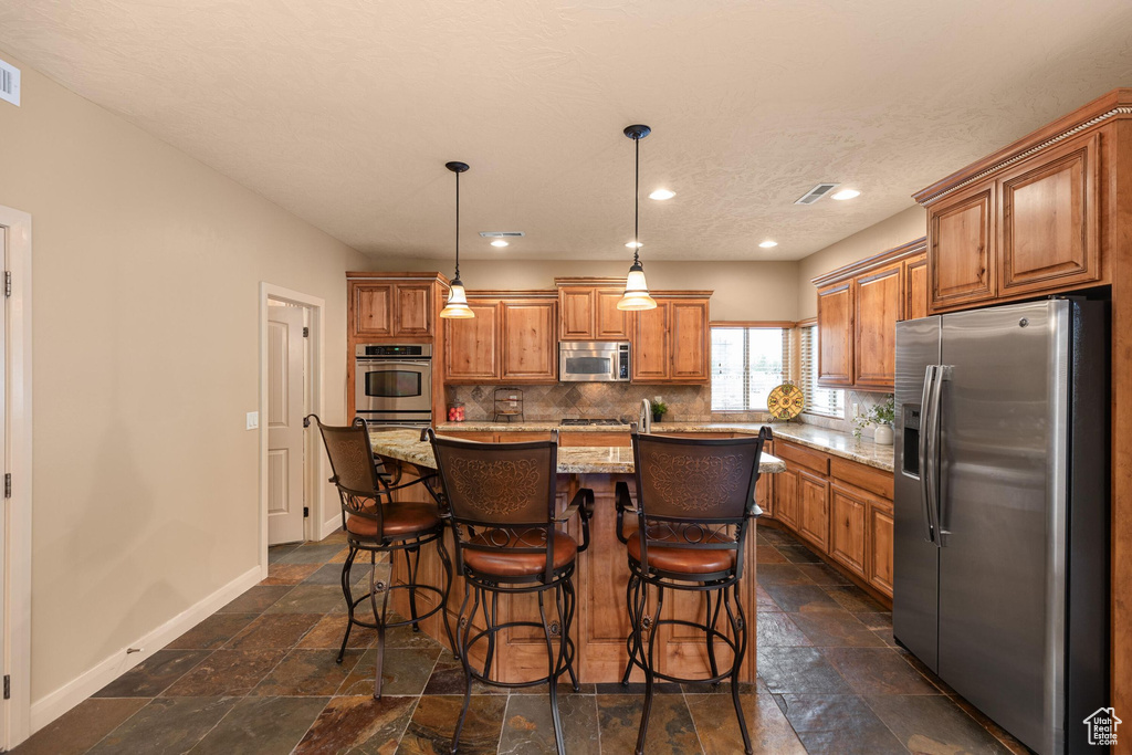 Kitchen featuring tasteful backsplash, baseboards, stone tile floors, brown cabinets, and stainless steel appliances