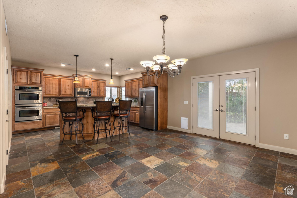 Kitchen featuring baseboards, french doors, brown cabinetry, a notable chandelier, and stainless steel appliances