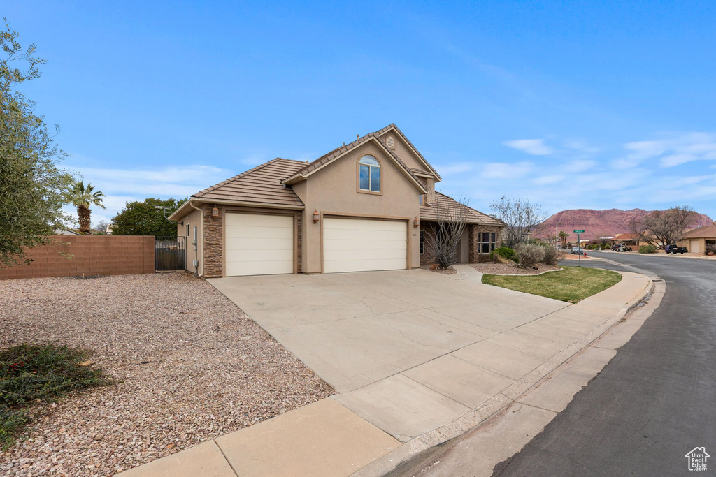 View of front of property with fence, a tile roof, stucco siding, a garage, and driveway