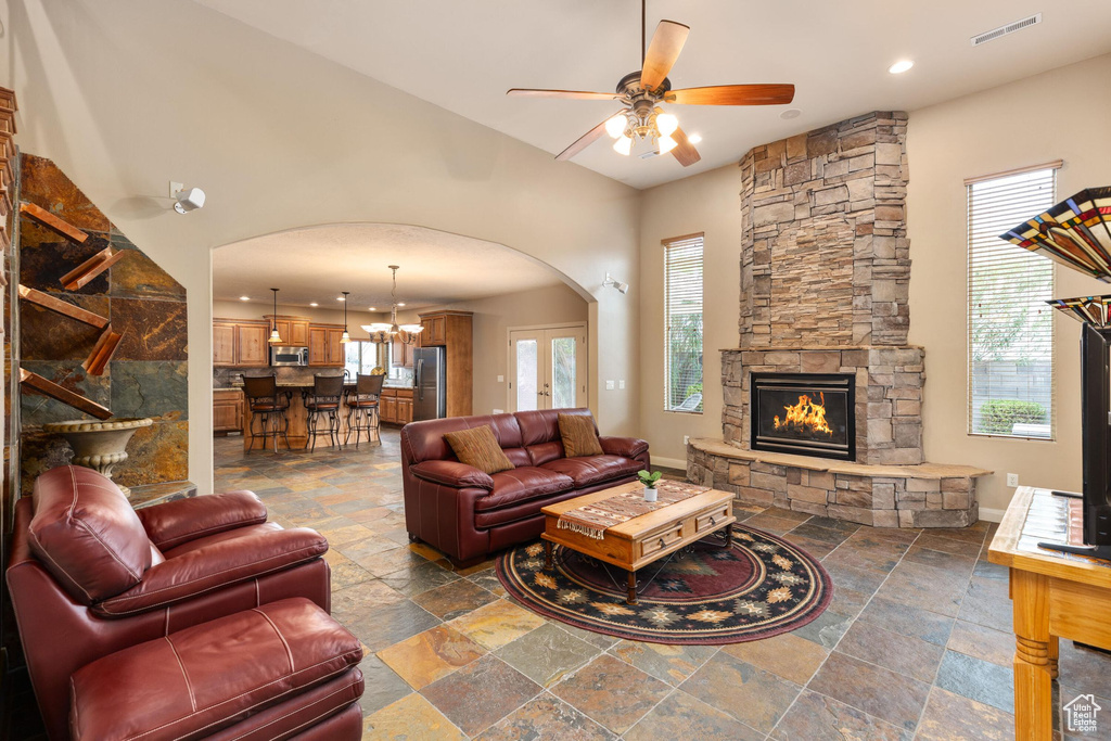 Living area with visible vents, ceiling fan with notable chandelier, stone tile floors, arched walkways, and a stone fireplace