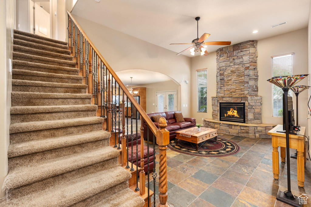 Living room with a ceiling fan, arched walkways, stone tile flooring, stairs, and a stone fireplace